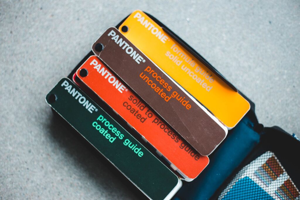 Guías de color Pantone abiertas en abanico con tonos naranja, amarillo y verde oscuro