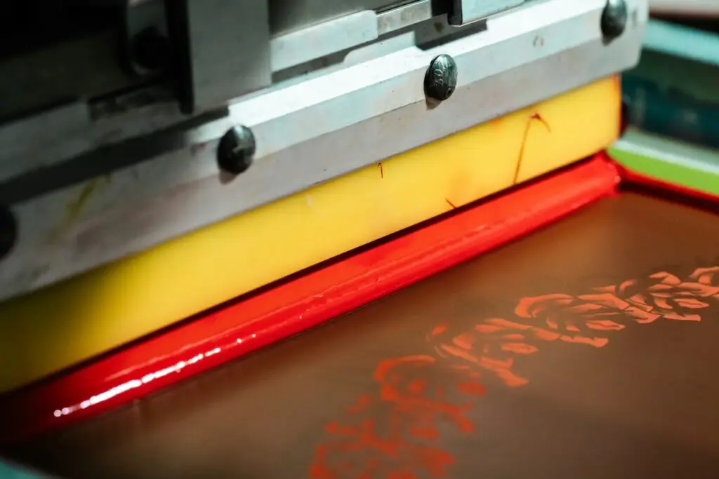 Rasqueta de una máquina de serigrafía plana depositando tinta roja sobre la pantalla